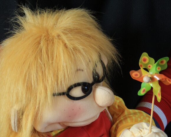 Die Therapiehandpuppe Max mit gelben Haaren und Windrad